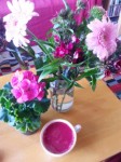 Cup of purple coloured soup pictured from above against big pink flowers