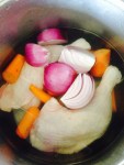 Raw high-welfare chicken and cut-up carrots and red onion covered with water in a pan