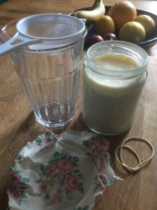 Kefir milk in a jar and plastic strainer over a second and clean jar. Cover and elastic band beside on kitchen worktop 