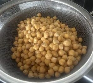 Cooked chickpeas drained in a sieve over a pan